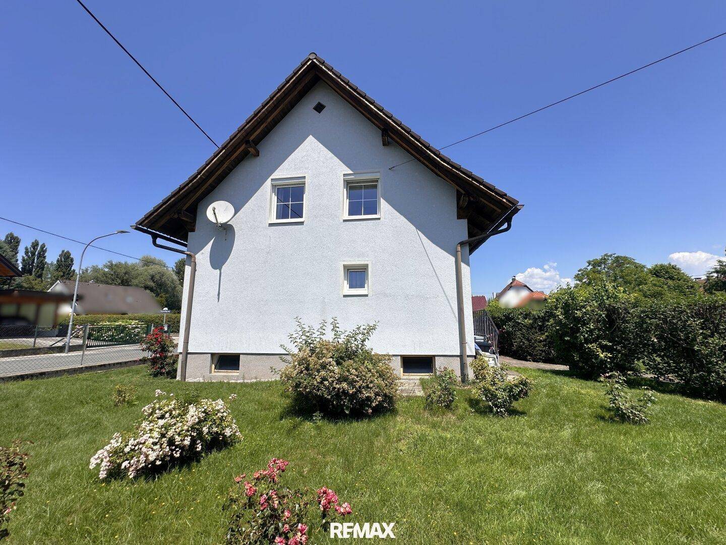 Das Einfamilienhaus präsentiert sich mit einer hellen Fassade und einem gepflegten Garten unter blauem Himmel.