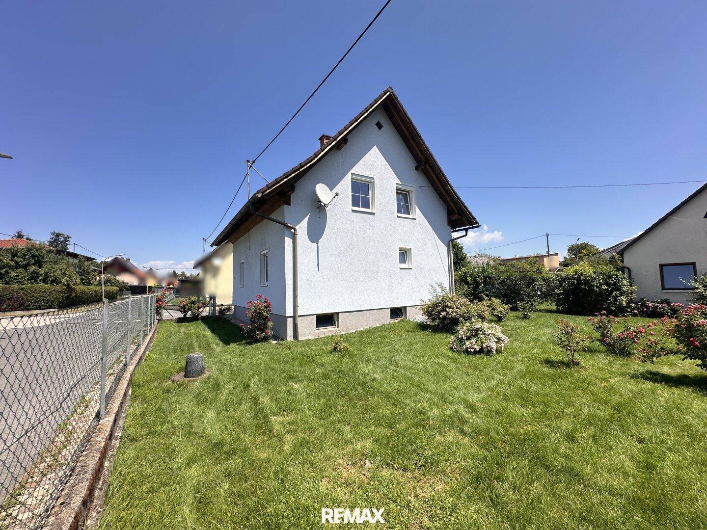 Das Haus mit weißer Fassade und braunem Dach ist von einem großen, sonnigen Garten umgeben.
