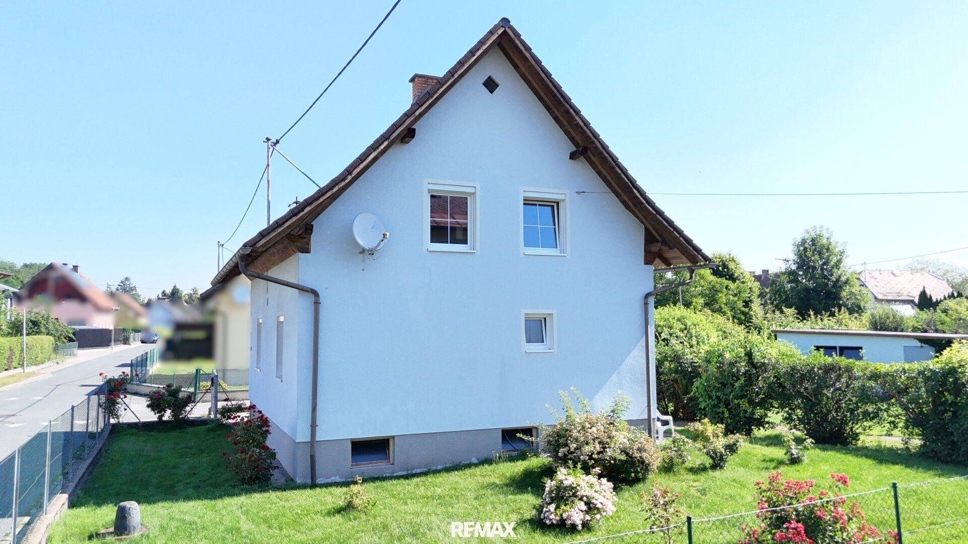 Seitenansicht des Einfamilienhauses mit weißer Fassade, Satteldach und grünem Gartenbereich.