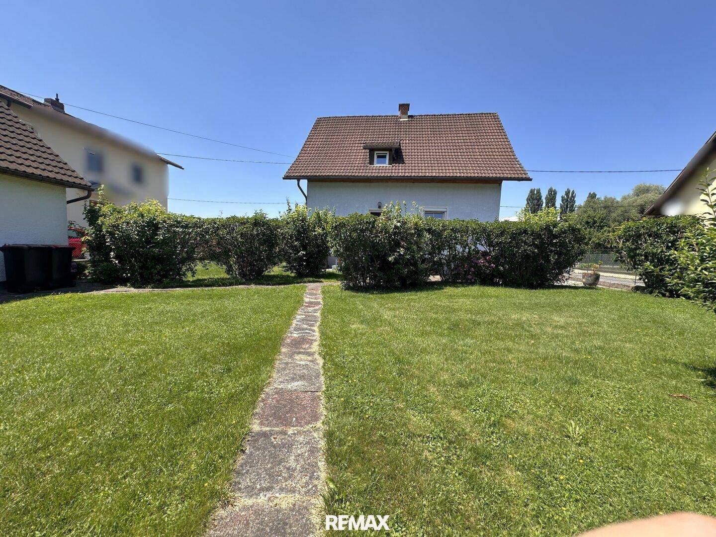 Gepflegter Garten mit Rasenfläche und einem Steinweg, der zum hinteren Teil des Hauses führt.