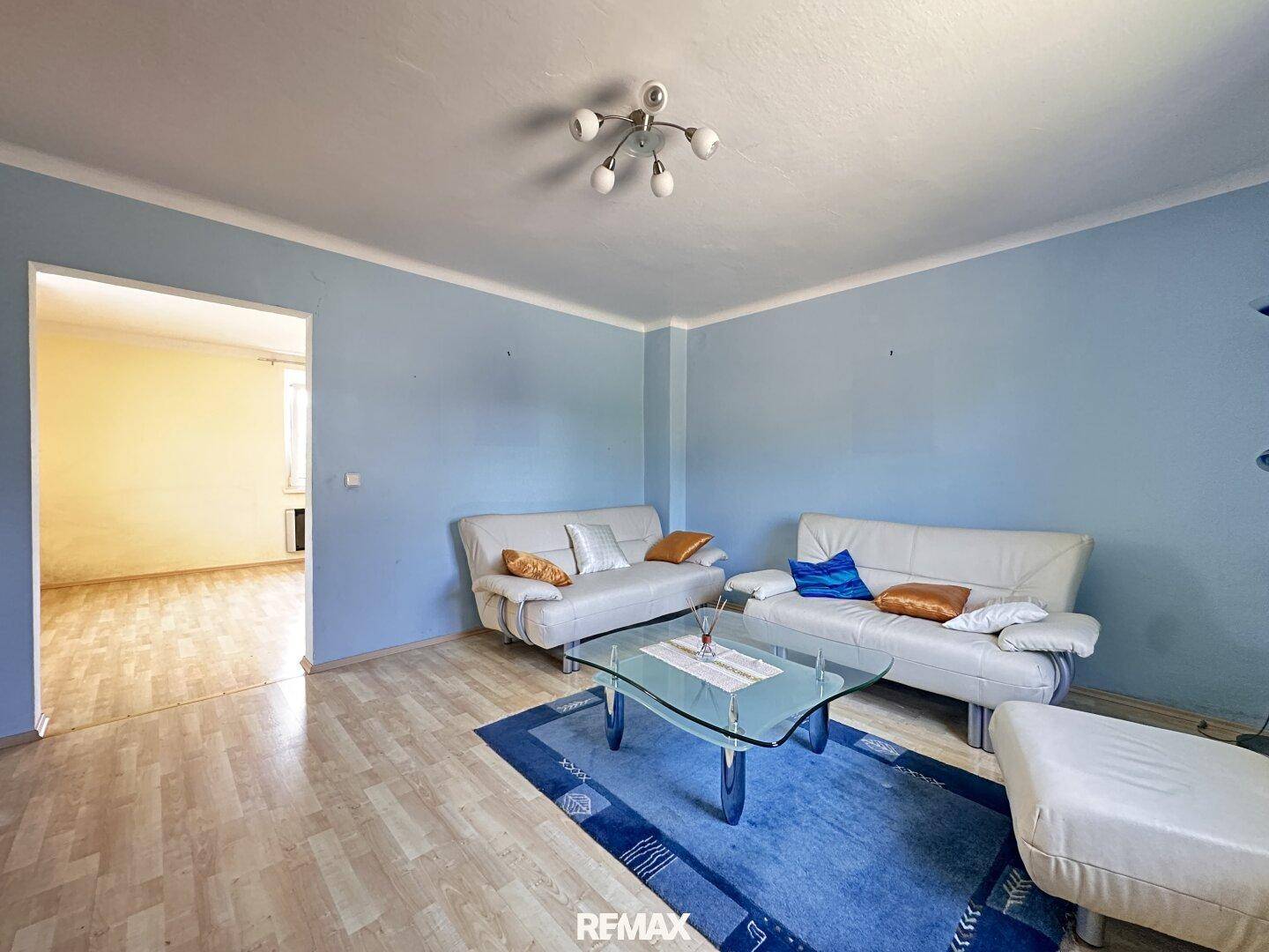 Helles Wohnzimmer mit blauen Wänden, Laminatboden und zwei weißen Sofas, bereit zur individuellen Gestaltung.