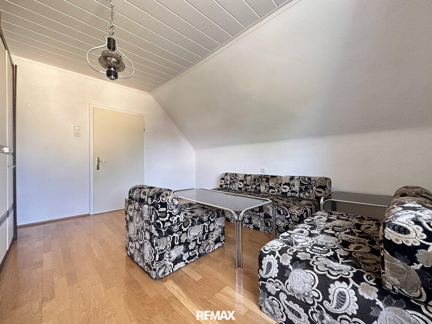 Dachgeschosszimmer mit schrägen Wänden, Holzboden und einer Tür, die zu weiteren Räumen führt.