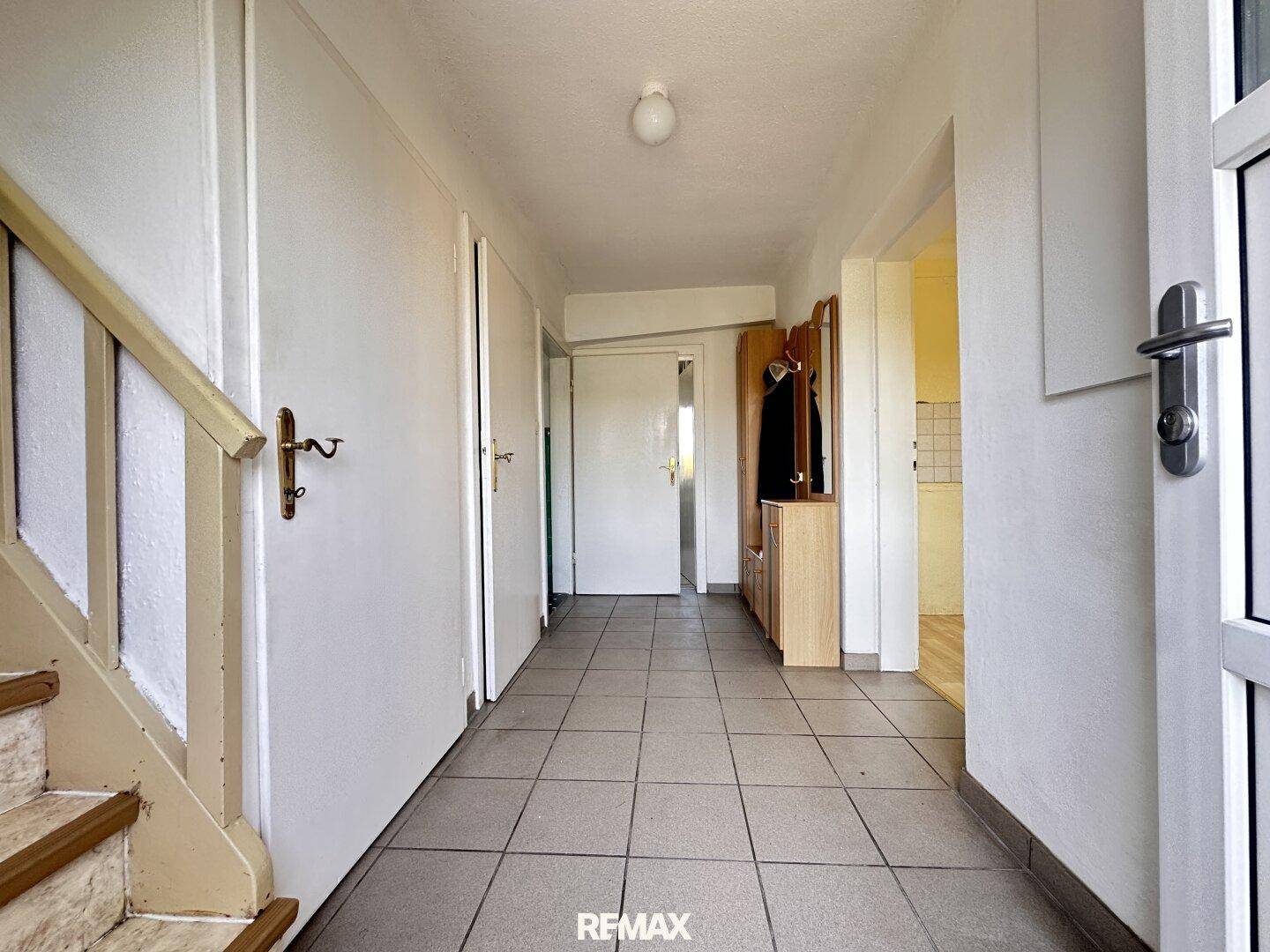 Heller Flur mit Fliesenboden, Treppenaufgang und Zugang zu verschiedenen Zimmern des Hauses.