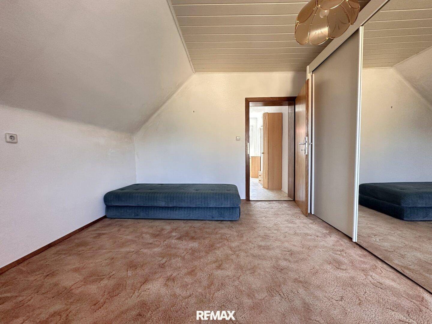Schlafzimmer im Dachgeschoss mit Teppichboden, schrägen Wänden und einem großen Spiegelschrank.