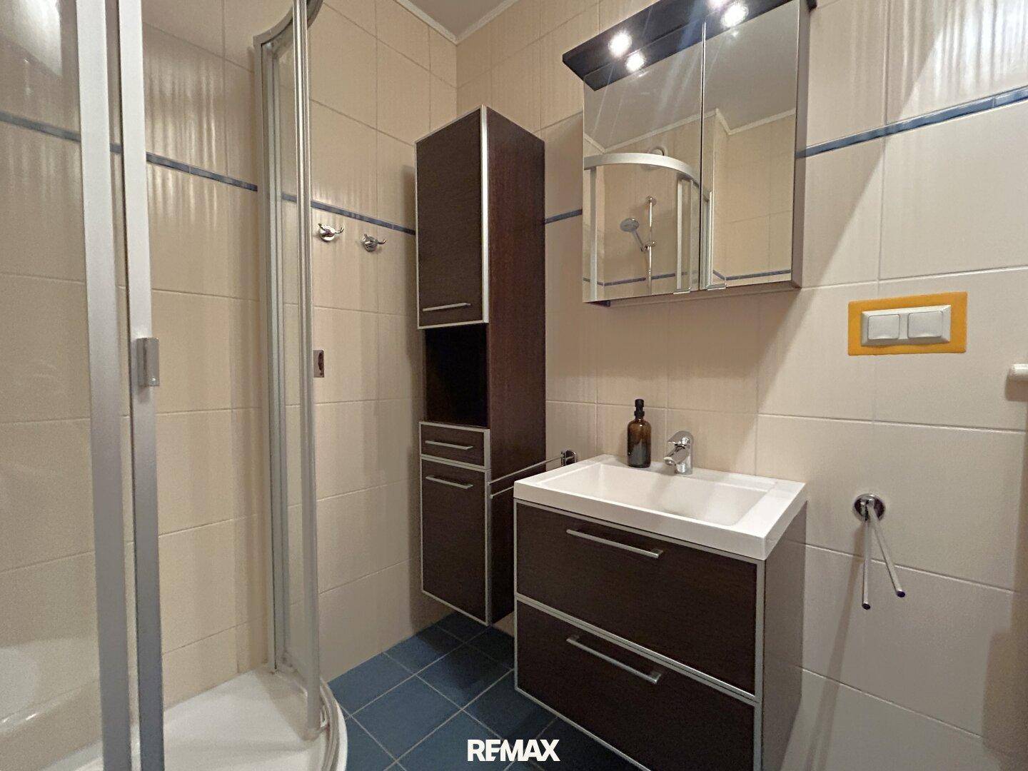 Funktionales Badezimmer mit Duschkabine, Waschbecken, Spiegelschrank und Fliesenboden.