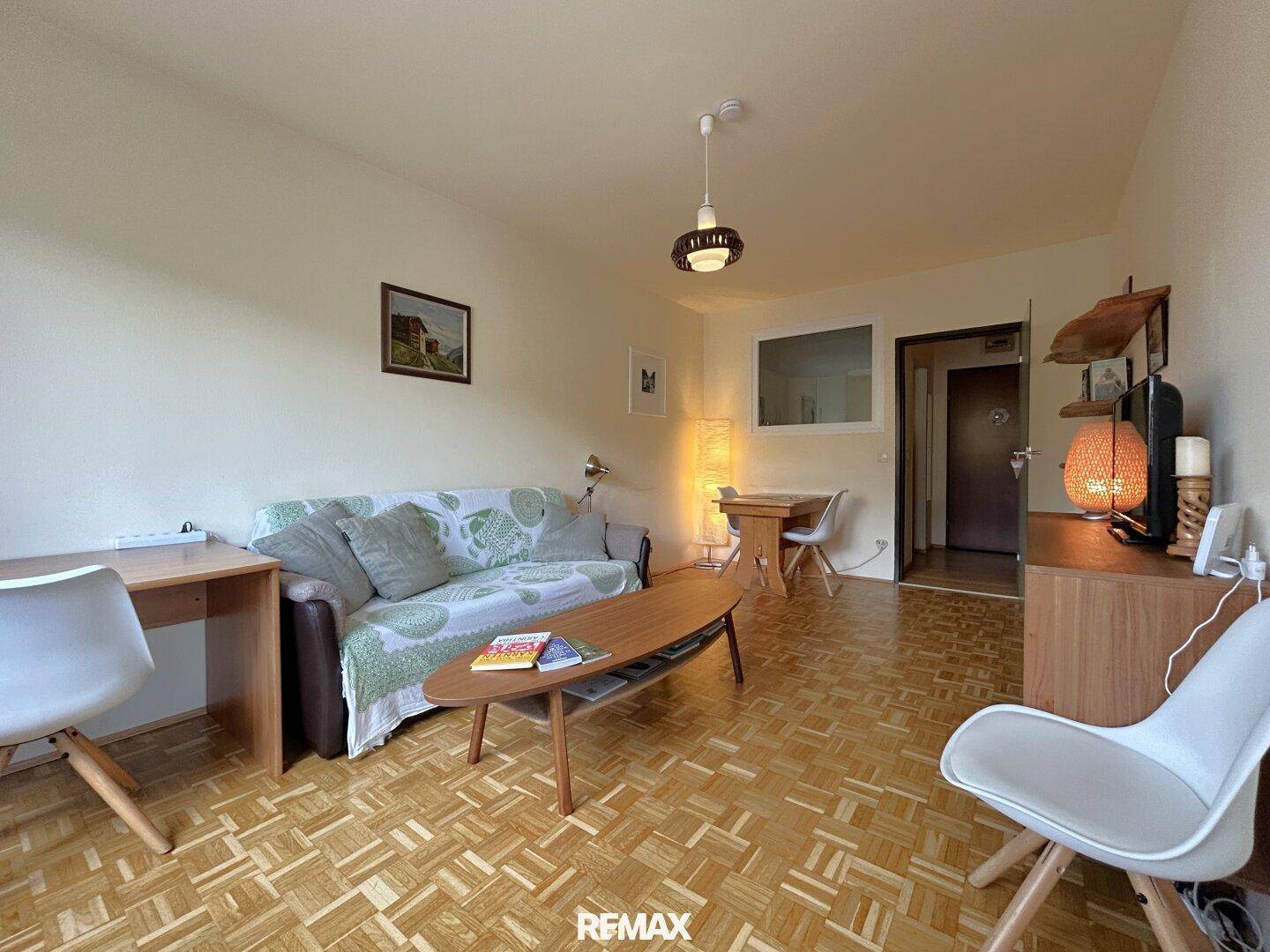 Gemütliches Wohnzimmer mit Parkettboden, Sofa und einem kleinen Essbereich im Hintergrund.