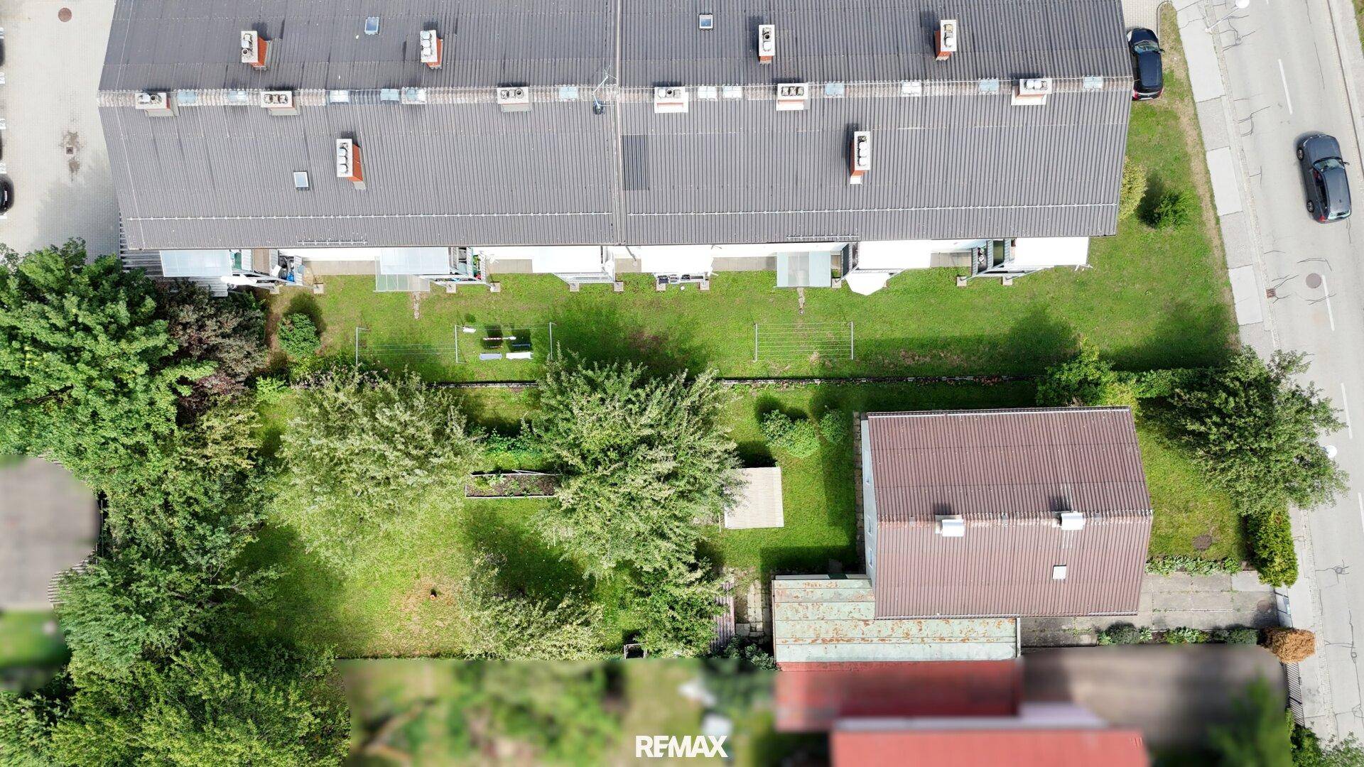 Draufsicht auf das Grundstück mit Garten, angrenzenden Häusern und Parkplätzen.