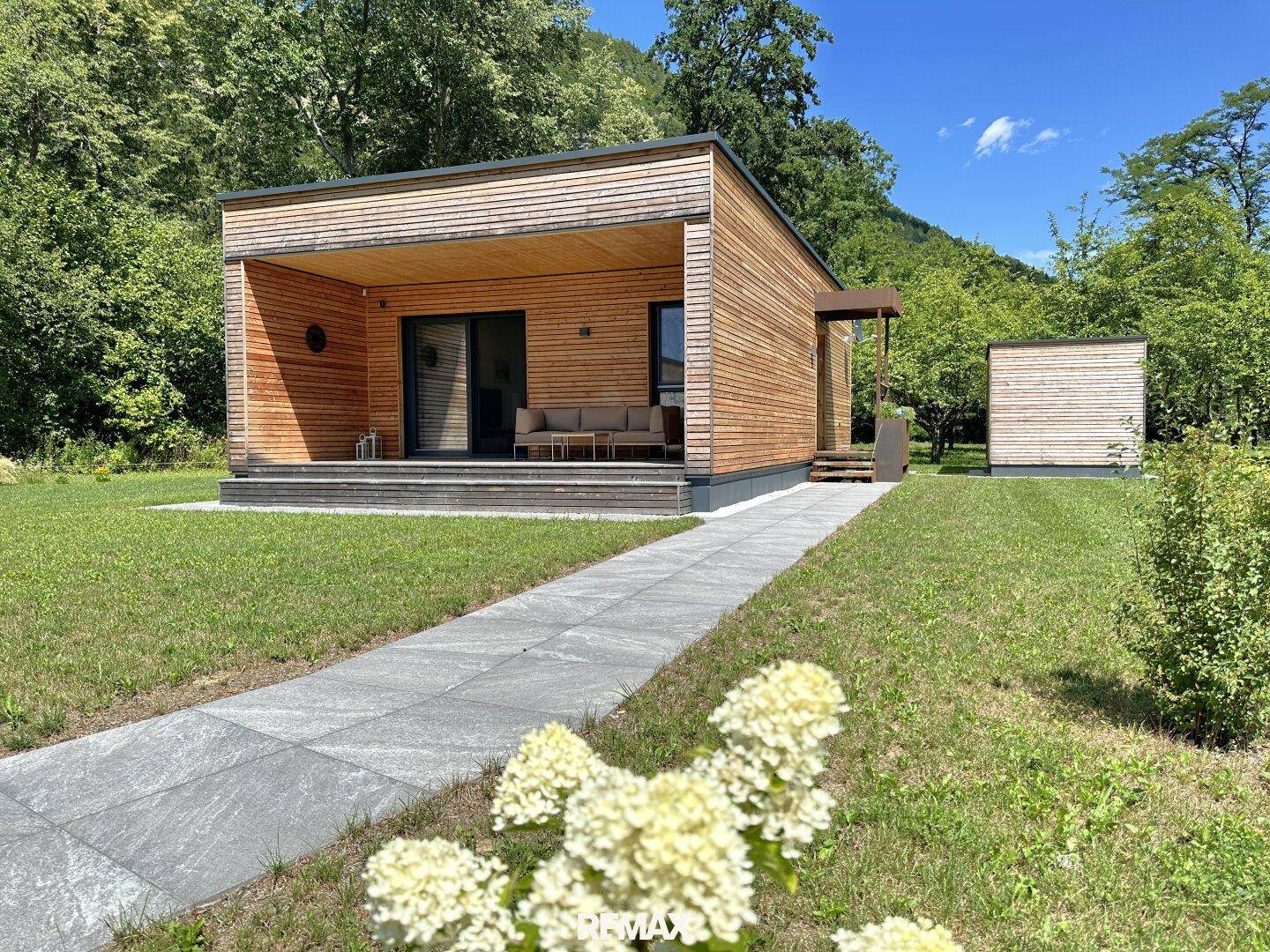 Zeitgenössisches Holzhaus mit großer überdachter Terrasse und Zugang zum weitläufigen Gartenbereich.