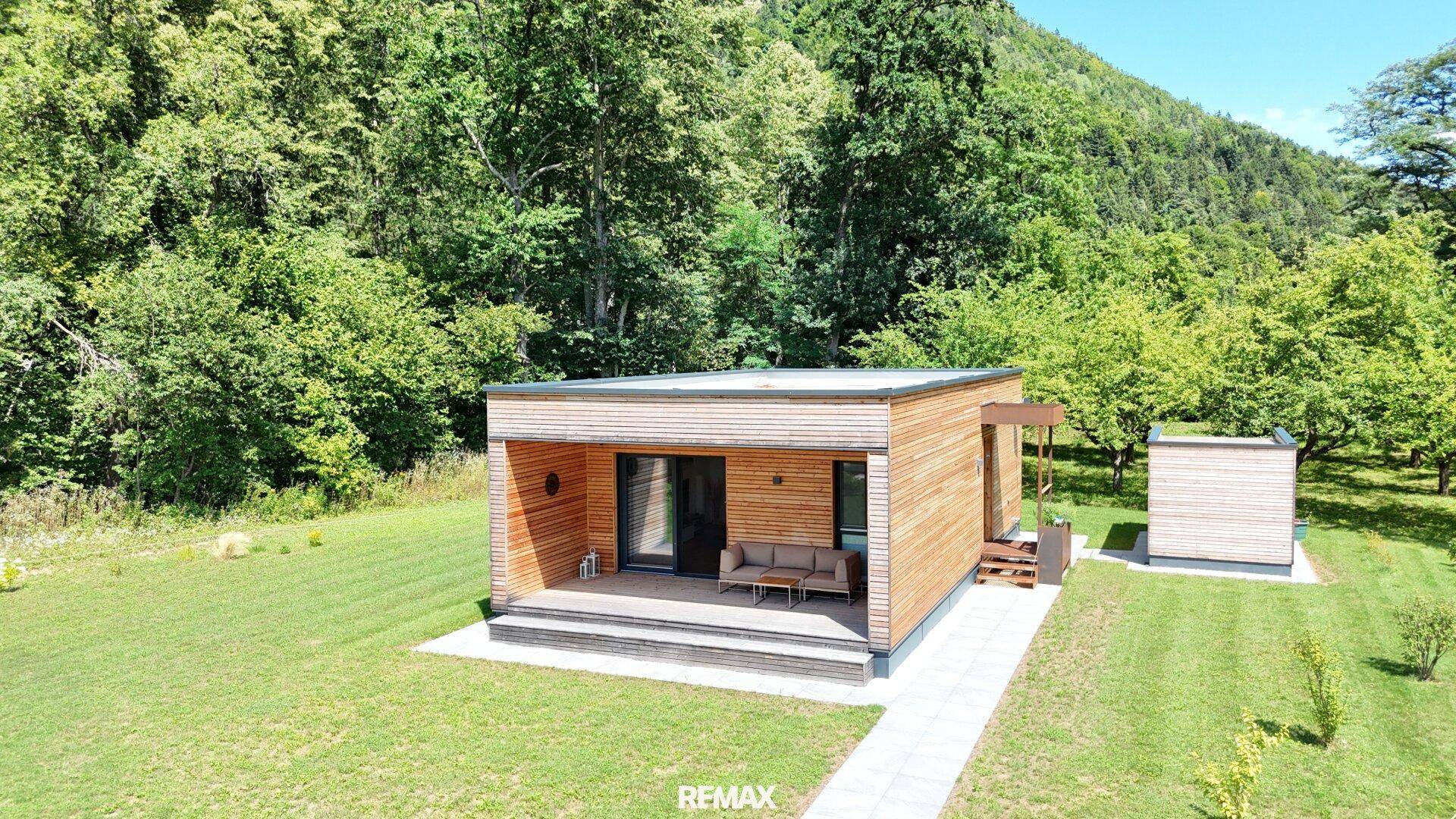 Vogelperspektive eines modernen Holzhauses mit Flachdach, umgeben von einem grünen Garten und Bäumen.