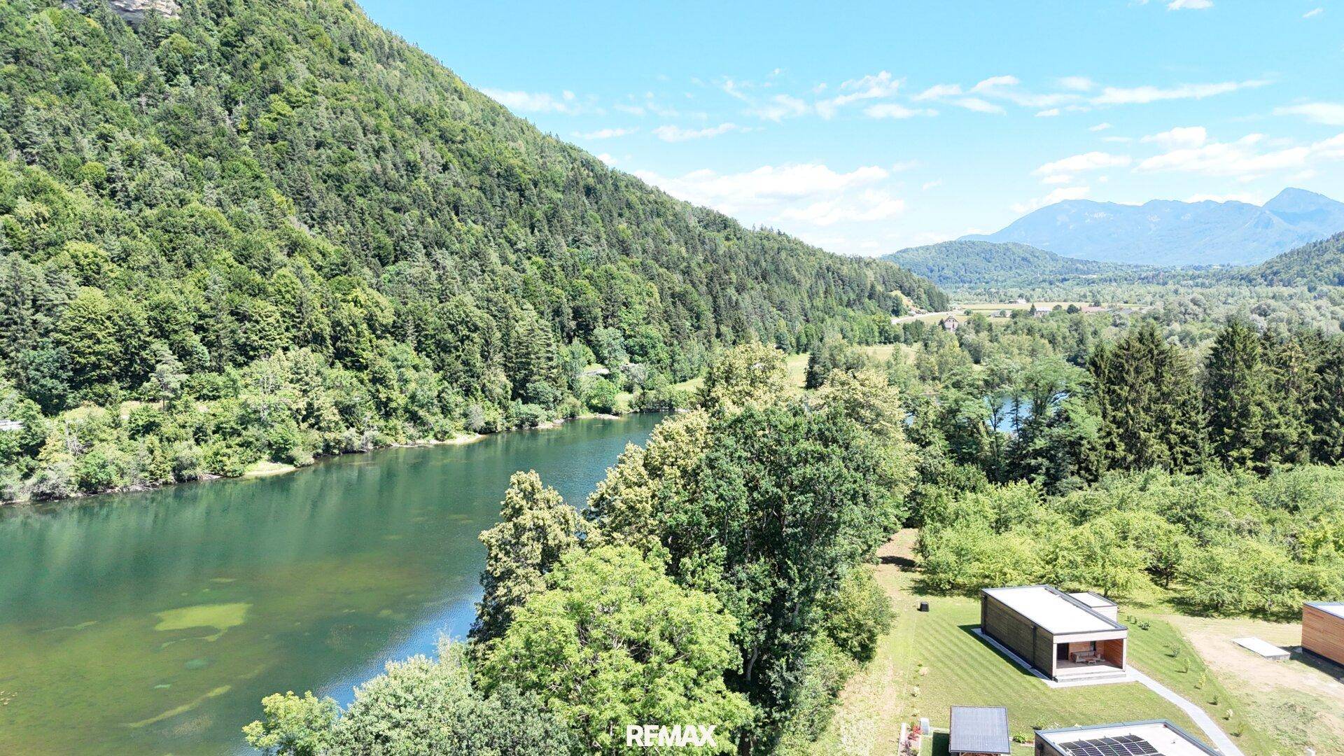 Weitläufige Landschaftsaufnahme mit Fluss, bewaldeten Bergen und vereinzelten modernen Häusern.