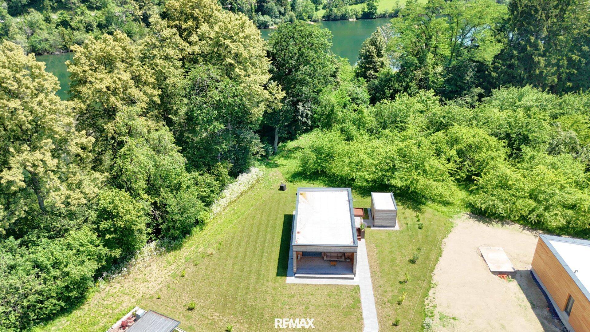 Einzelnes modernes Holzhaus mit Flachdach und Garten, umgeben von Bäumen und Flussblick.
