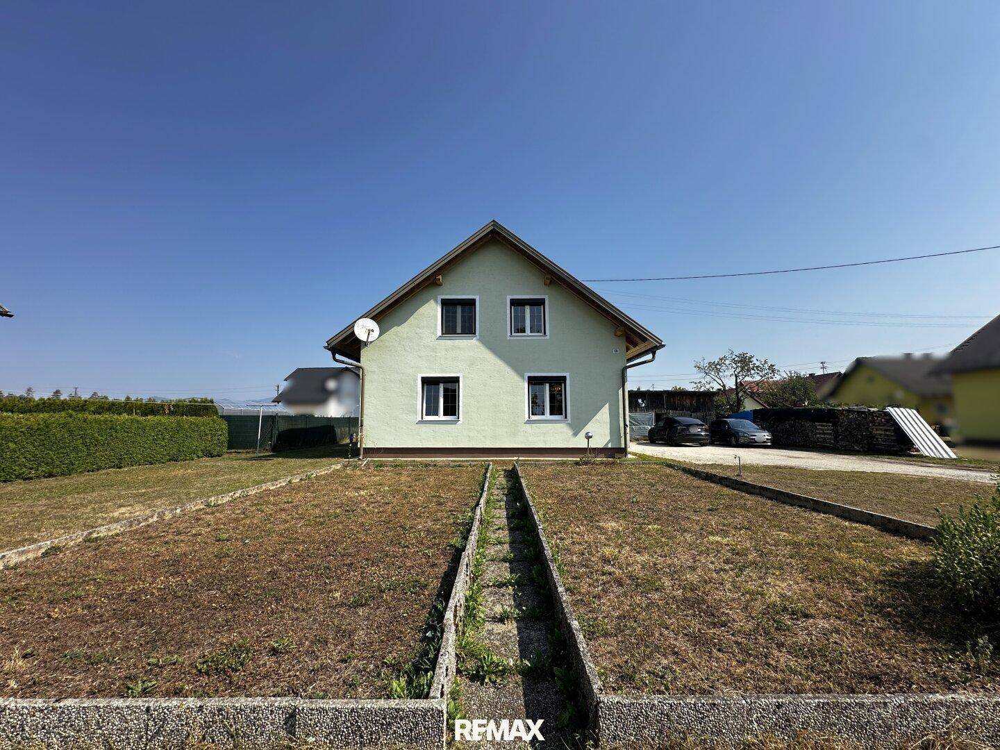 Vorderansicht des Hauses mit hellgrüner Fassade und einem trockenen Gartenbereich unter blauem Himmel.