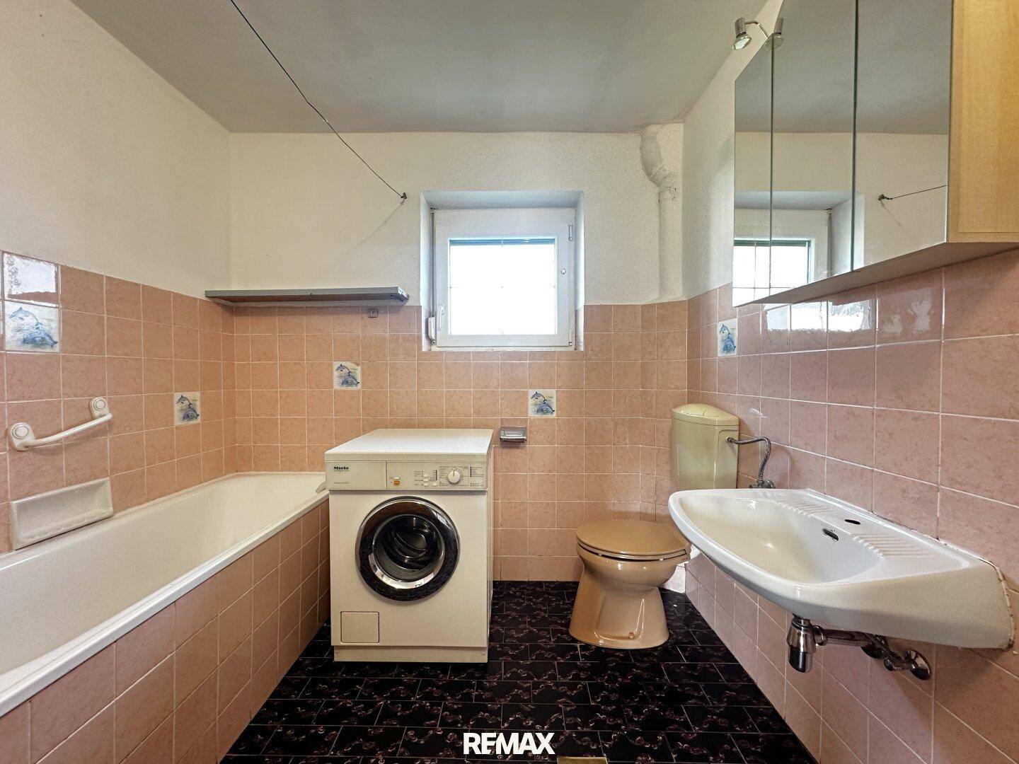 Badezimmer mit rosa Fliesen, Badewanne, WC, Waschbecken und Waschmaschine, im Stil der 80er Jahre.