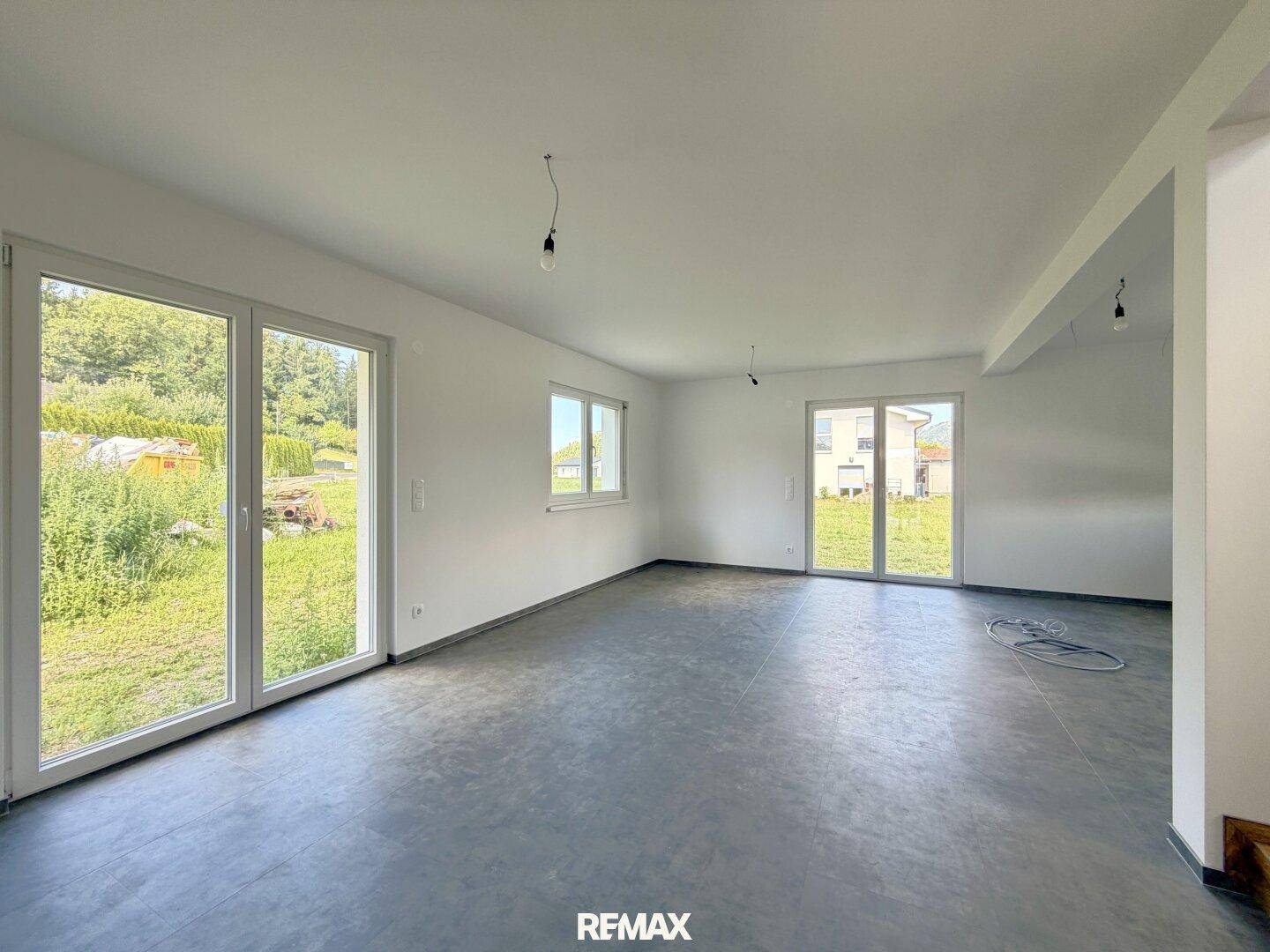 Heller, unmöblierter Wohnbereich mit zwei großen Fenstertüren und Blick ins Grüne.