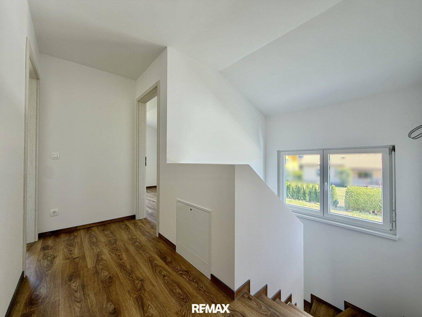 Heller Flur mit Holztreppe und Fenster, das Tageslicht in den oberen Bereich bringt.