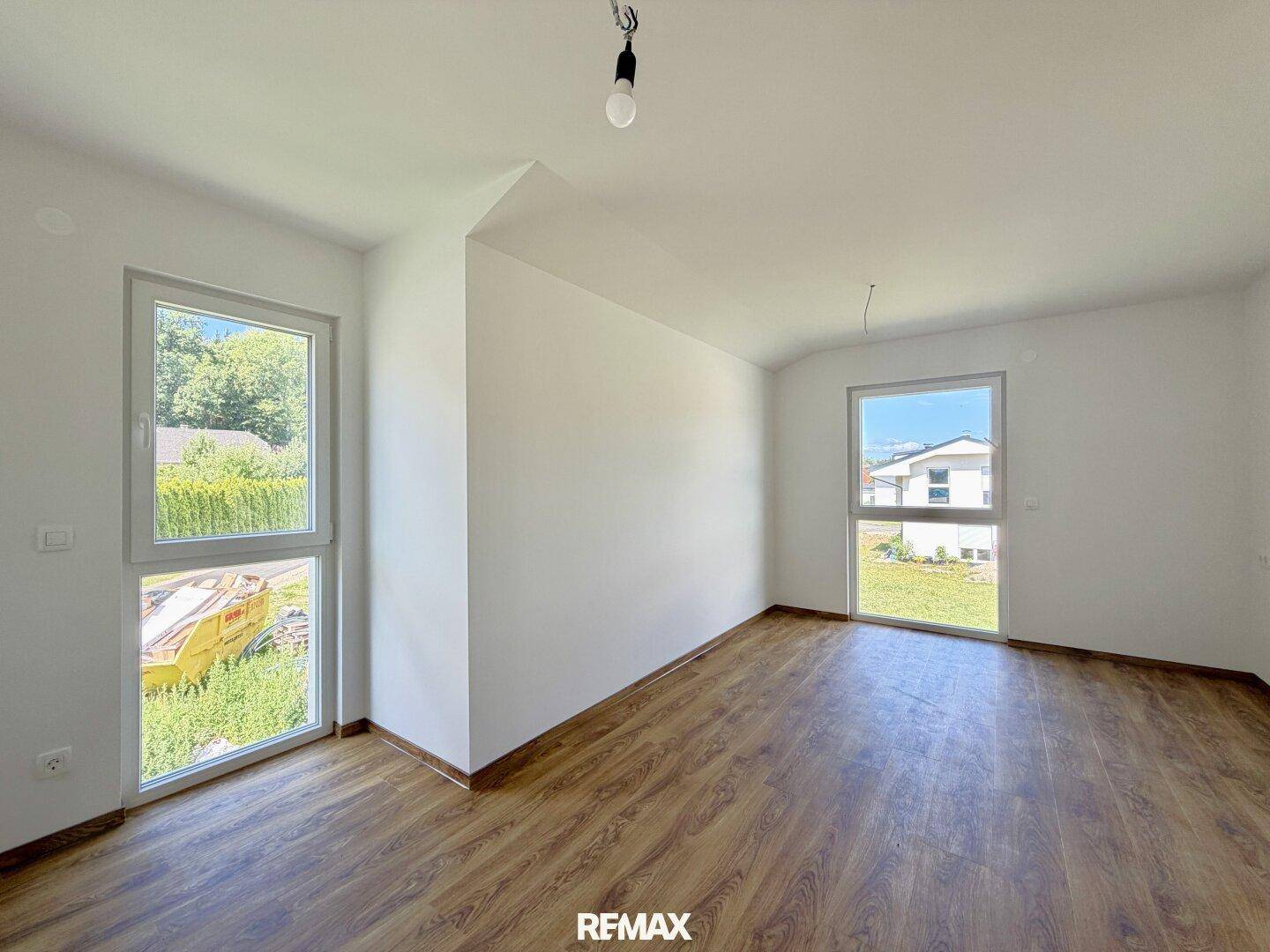 Geräumiges, unmöbliertes Zimmer mit zwei großen Fenstern und Holzboden.