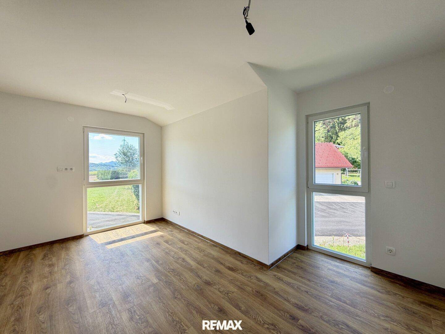 Lichtdurchflutetes, unmöbliertes Zimmer mit zwei Fenstern und Holzboden.