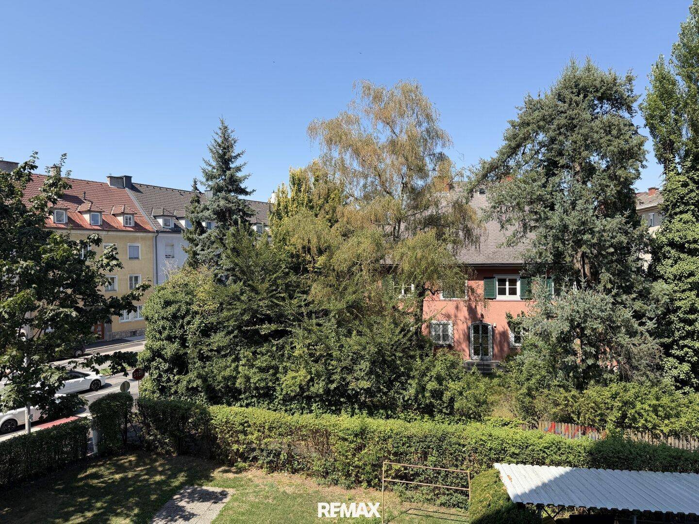 Grüner Gartenbereich mit Bäumen und Hecken, umgeben von Wohngebäuden.