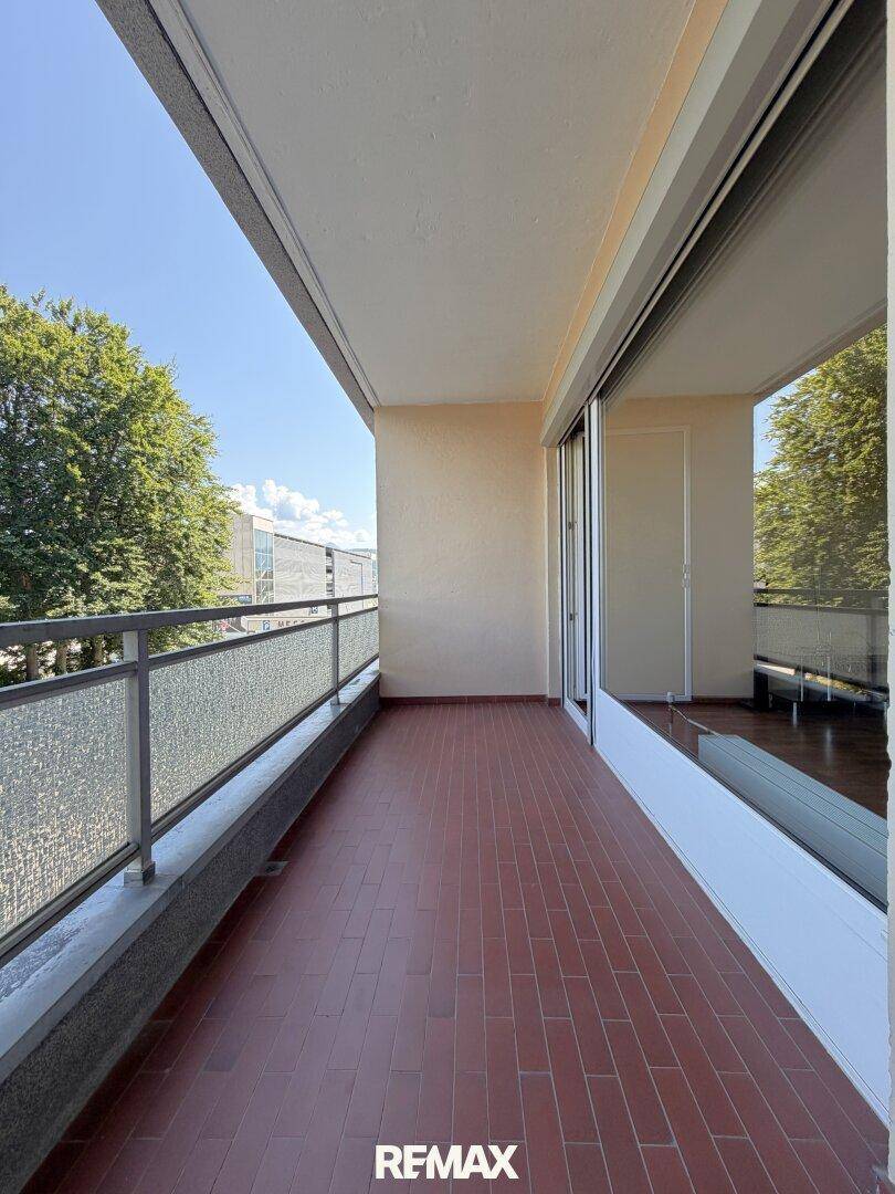 Langer Balkon mit Fliesenboden und Glasbrüstung, bietet einen sonnigen Außenbereich.