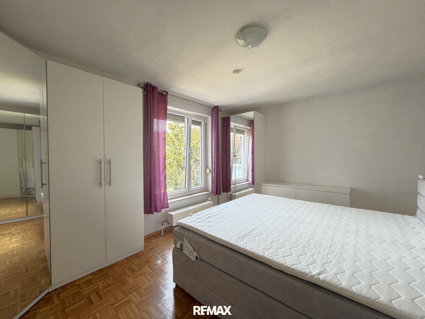 Schlafzimmer mit Parkettboden, großem Bett und weißen Kleiderschränken mit Spiegelfront.