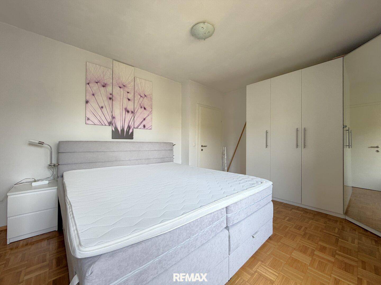 Schlafzimmer mit Doppelbett, Nachttisch und weißem Kleiderschrank mit Spiegeltür.