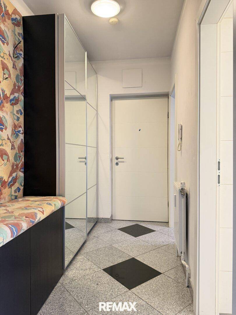 Eingangsbereich mit Fliesenboden, Spiegelschrank und weißer Eingangstür.
