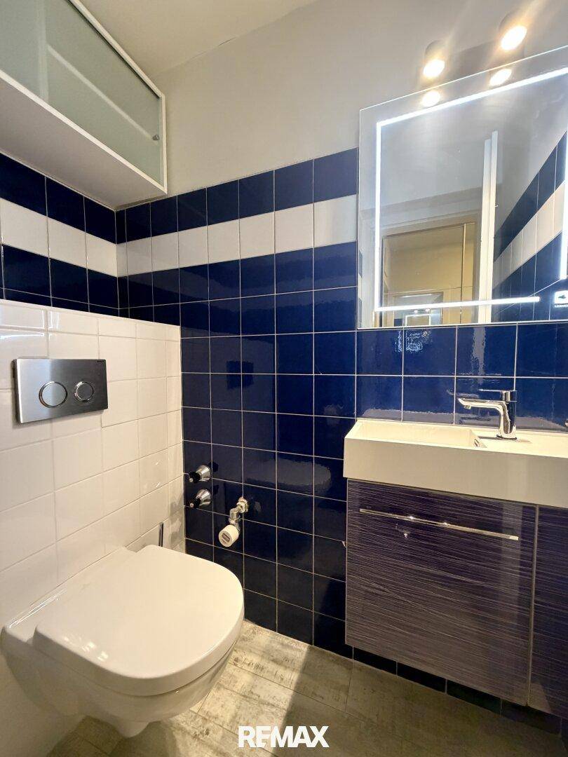Gäste-WC mit blauen und weißen Fliesen, wandhängendem WC und modernem Waschbecken.