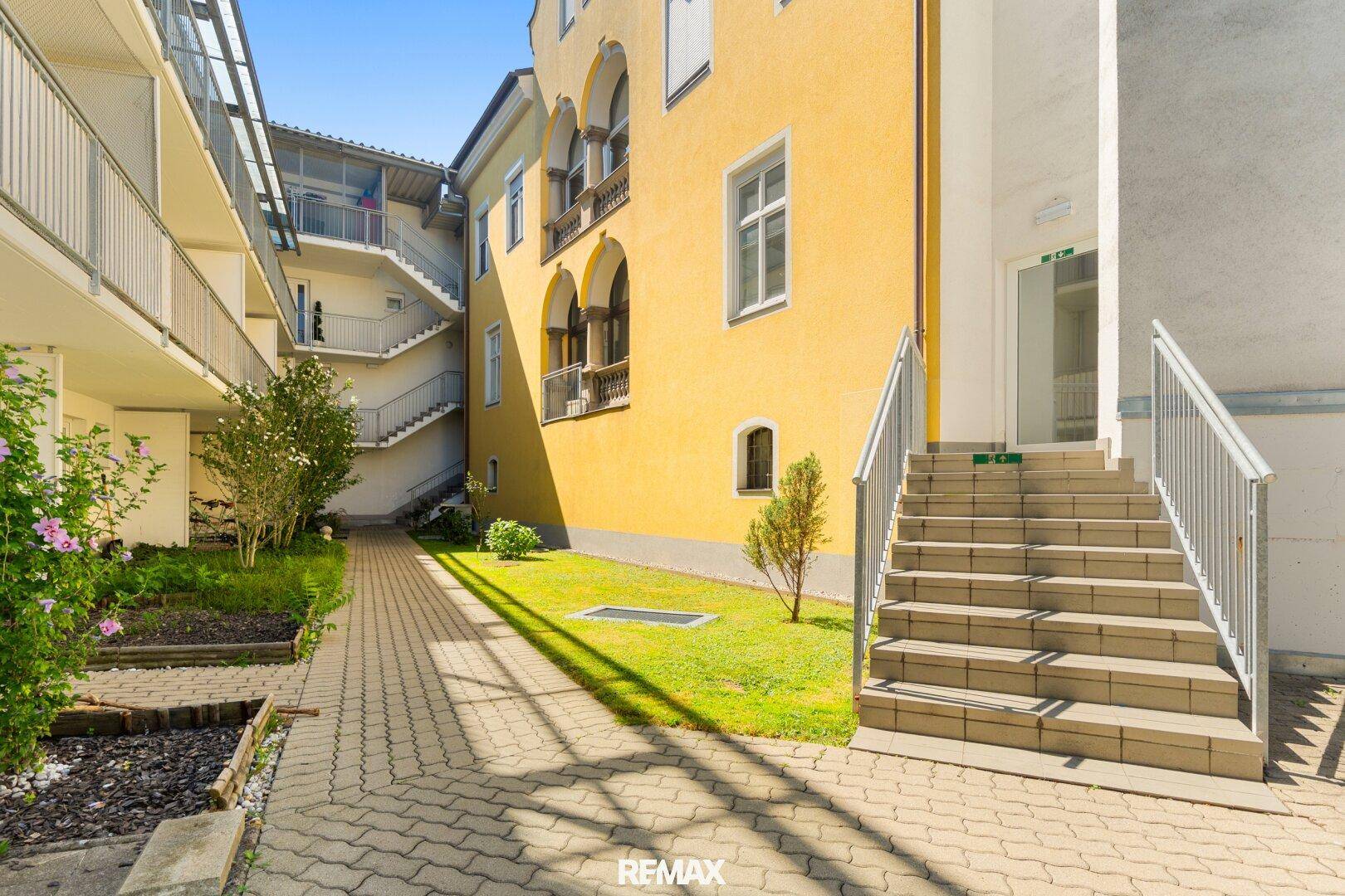 Außenansicht des Gebäudes mit gepflegtem Innenhof, Grünflächen und Zugangstreppen.