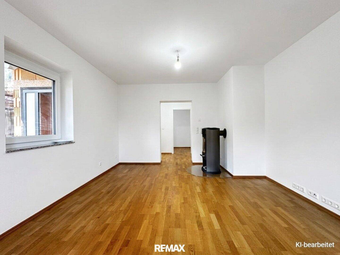 Geräumiges Wohnzimmer mit Holzboden, weiß gestrichenen Wänden und Kaminofen.
