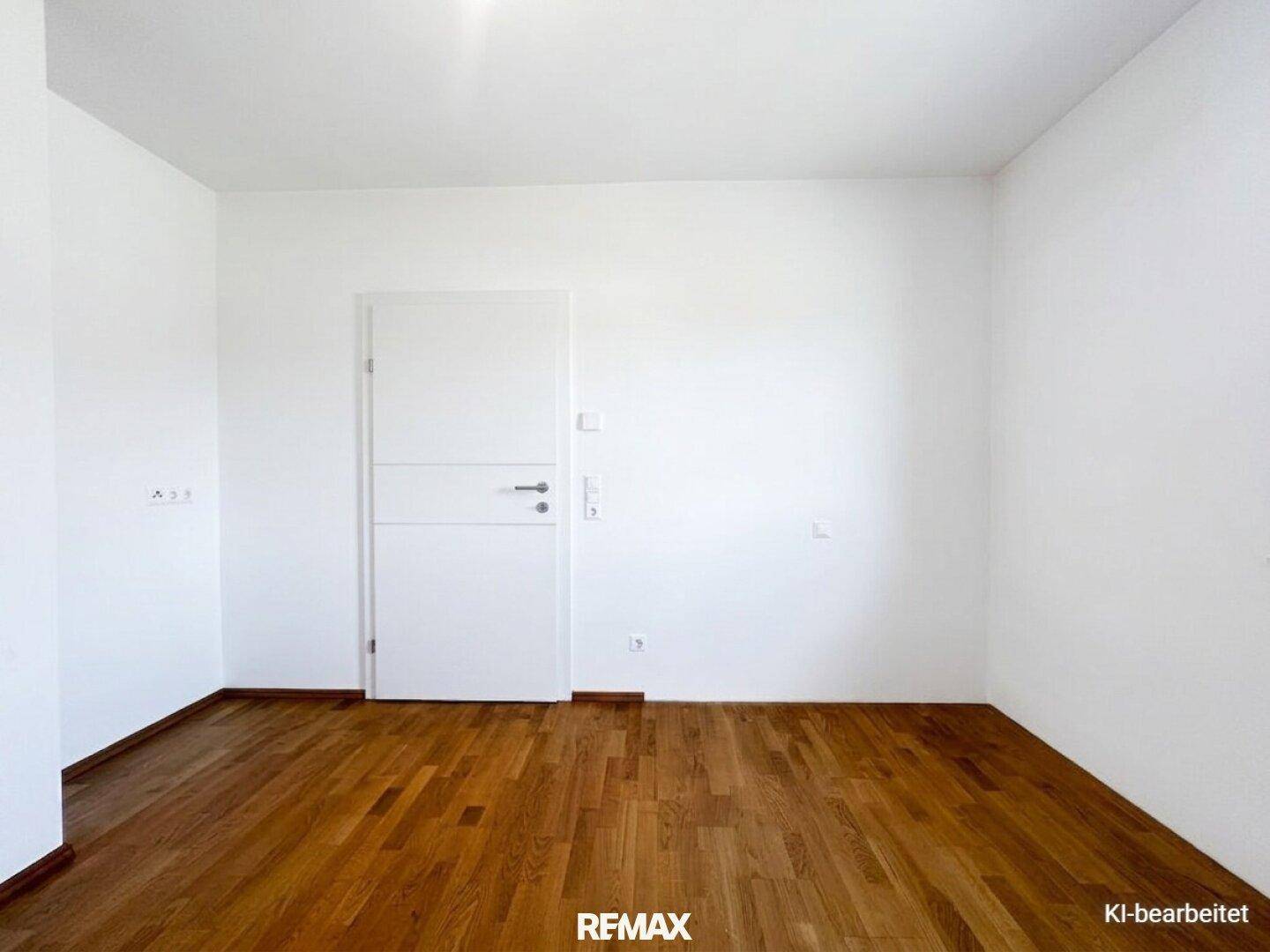 Leerer Raum mit Holzboden, weißen Wänden und einer modernen Innentür.