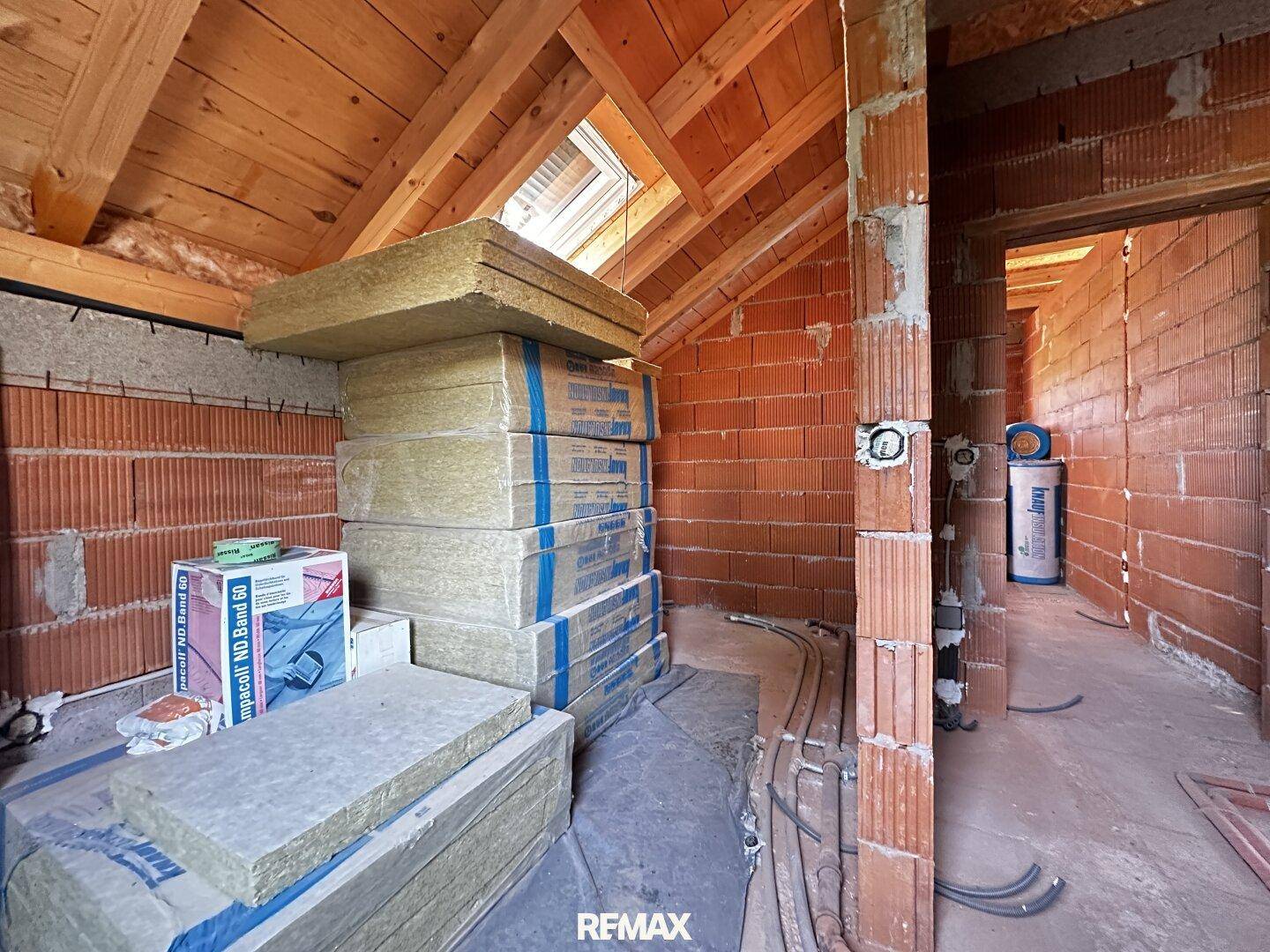 Dachgeschoss im Rohbau mit Dämmmaterial, sichtbaren Holzbalken und Dachfenster.