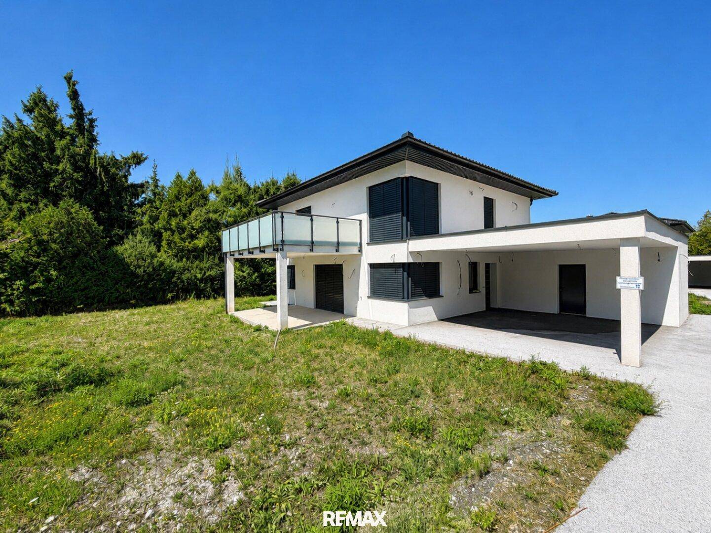 Modernes Einfamilienhaus mit Balkon und Carport, umgeben von viel Grün und Natur.