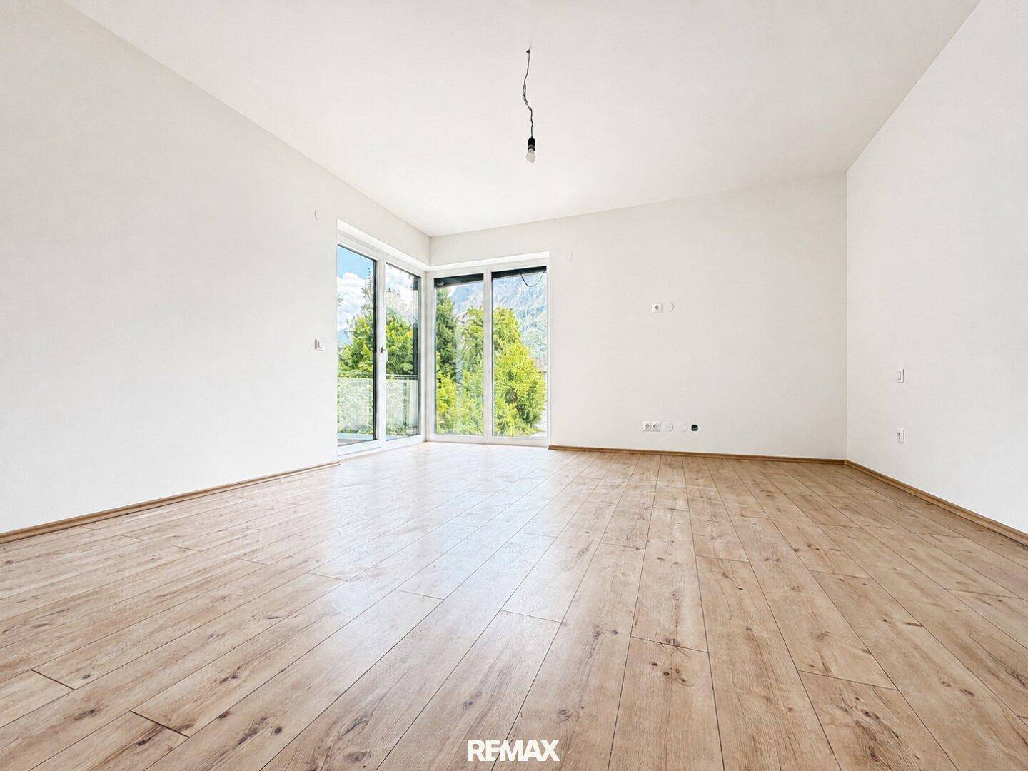 Helles, unmöbliertes Schlafzimmer mit Holzboden und großen Fenstern zum Außenbereich.