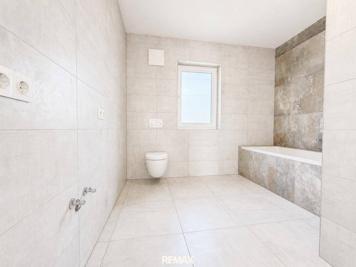 Geräumiges, unmöbliertes Badezimmer mit Badewanne, Wand-WC und Fenster.