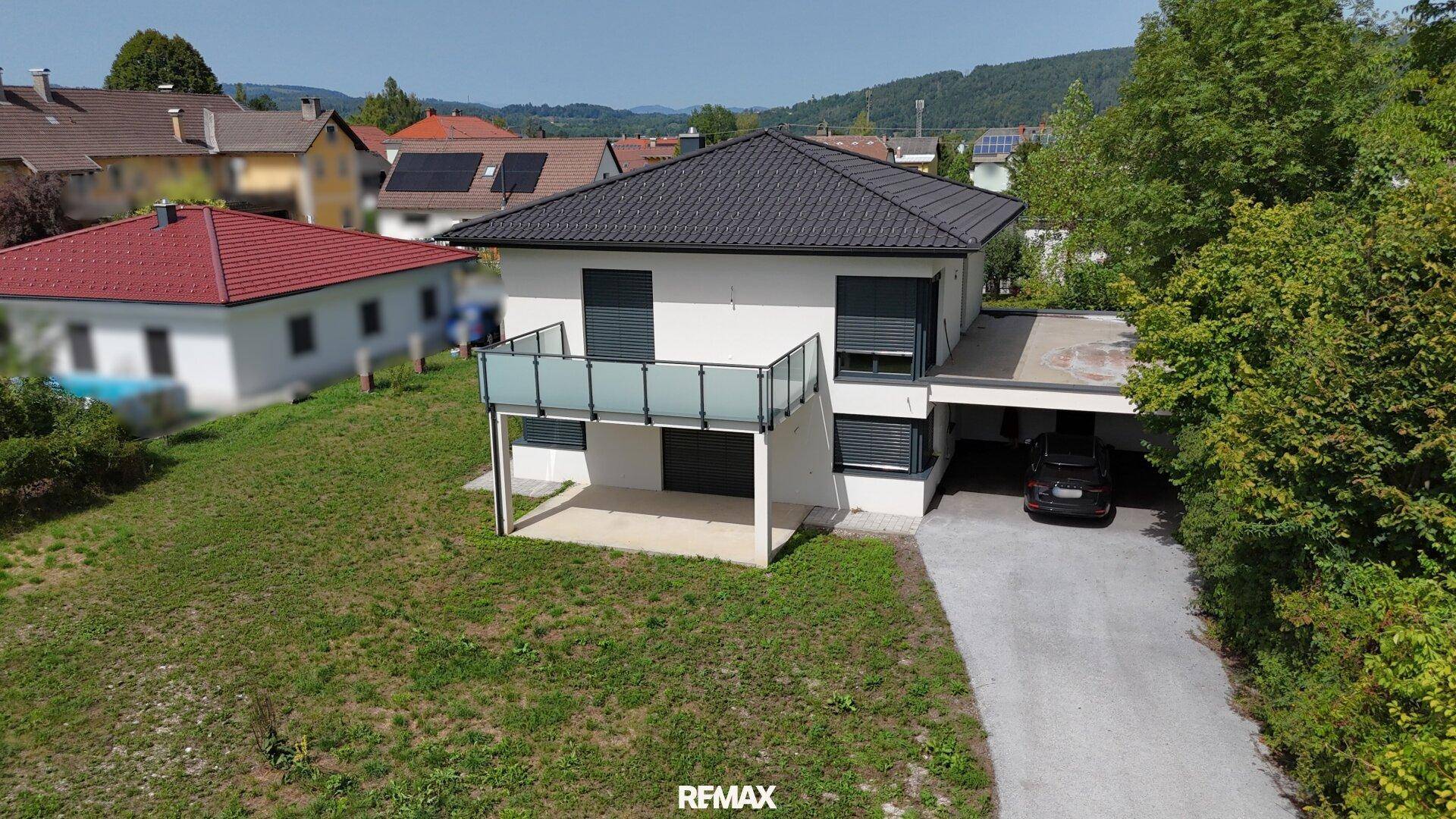 Freistehendes Einfamilienhaus mit Balkon, Carport und Zufahrt in ländlicher Umgebung.