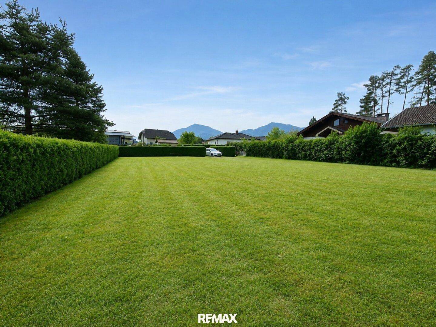 Große Rasenfläche mit gepflegter Hecke und Bergblick im Hintergrund.