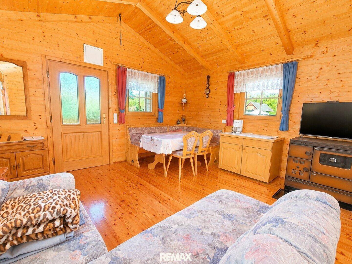 Gemütlicher Wohn- und Essbereich in einer Holzhütte mit traditionellem Ofen und bunten Vorhängen.