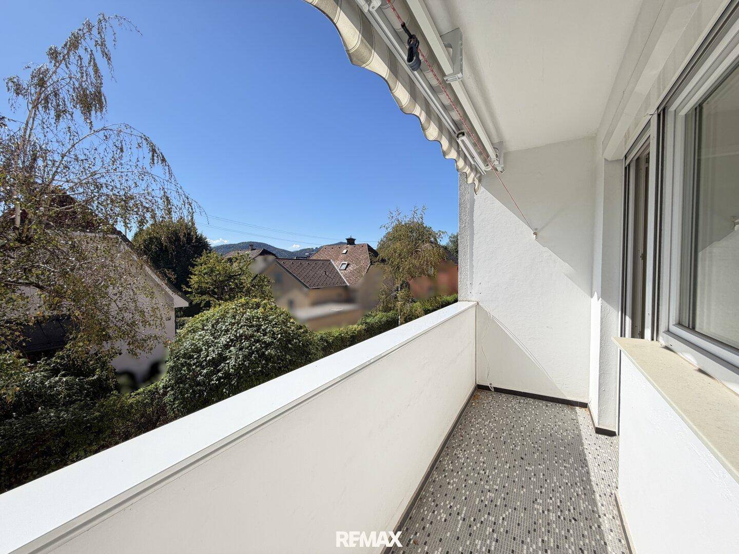 Heller Balkon mit Markise und Blick auf die umliegende Wohngegend und Berge.