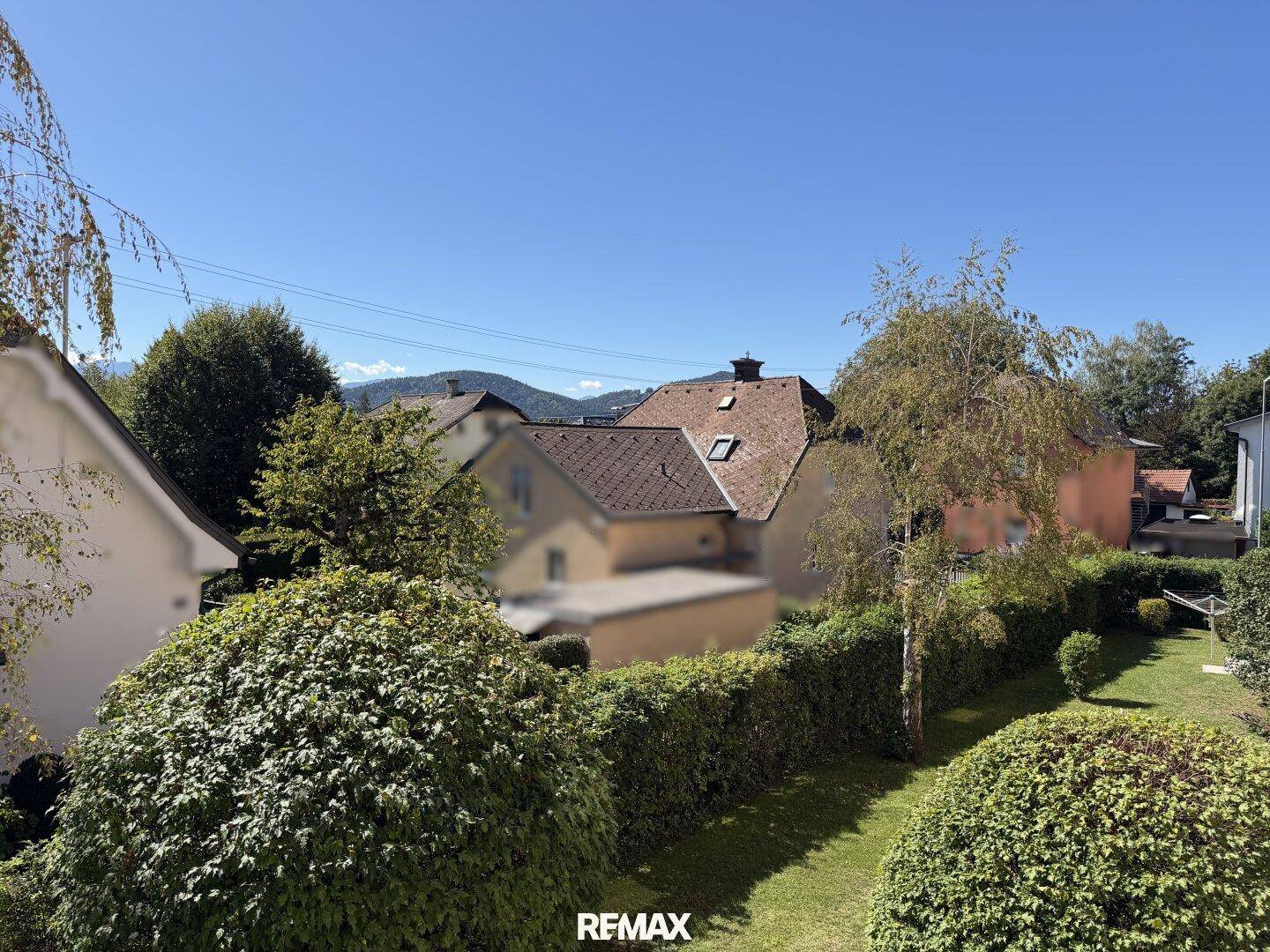 Weitläufige Aussicht auf grüne Gärten, benachbarte Häuser und die Berglandschaft.