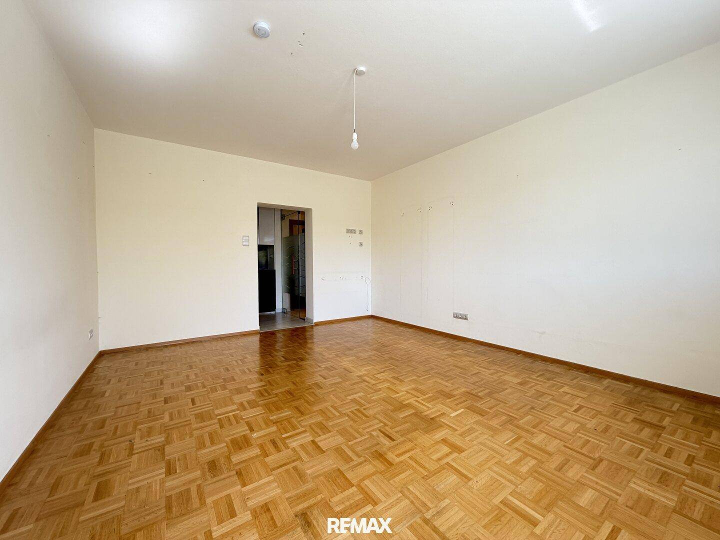 Geräumiges Zimmer mit klassischem Parkettboden und weiß gestrichenen Wänden.