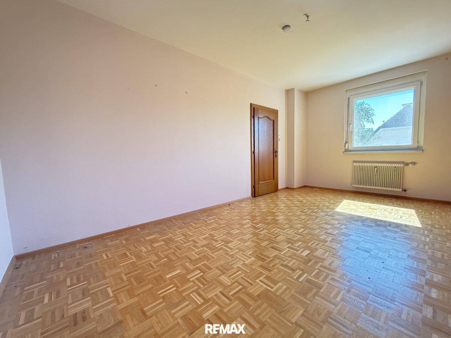 Ruhiges Zimmer mit Parkettboden, Fenster und einer Holztür.