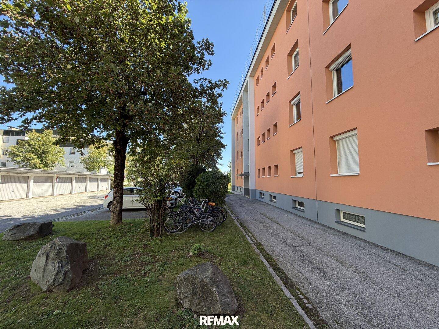 Außenansicht eines Mehrfamilienhauses mit Parkplätzen und Bäumen im Vordergrund.