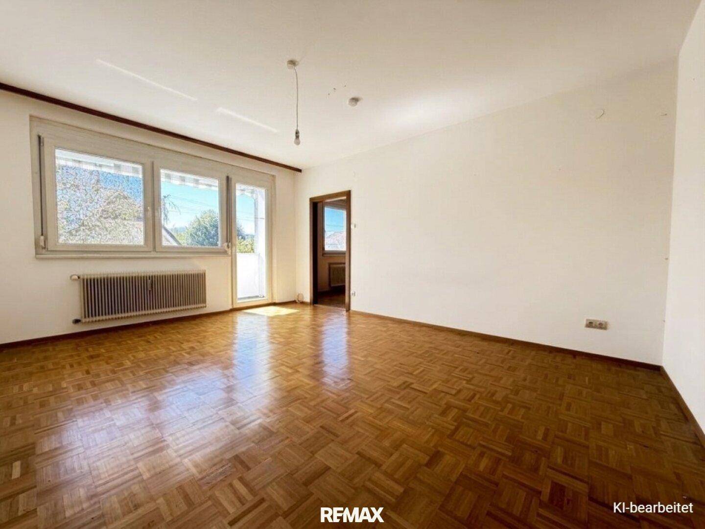 Helles Wohnzimmer mit Parkettboden, großem Fenster und Zugang zum Balkon.