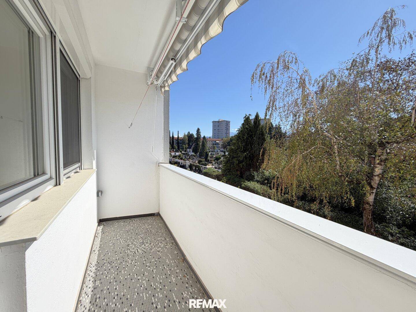 Geräumiger Balkon mit Markise und weitem Blick über grüne Bäume und die Stadt.