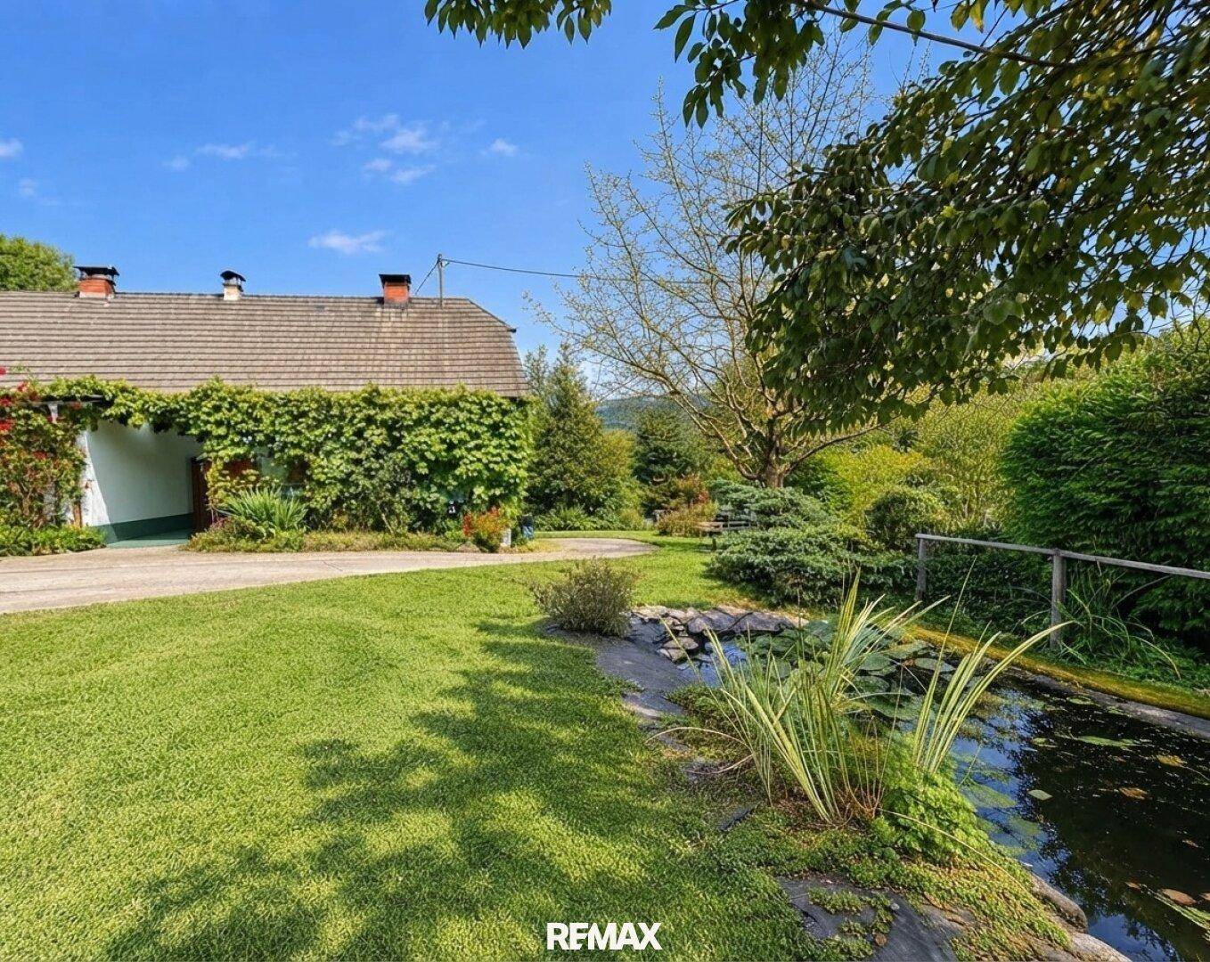 Gepflegter Gartenbereich mit Teich, üppiger Vegetation und Blick auf das Wohnhaus.