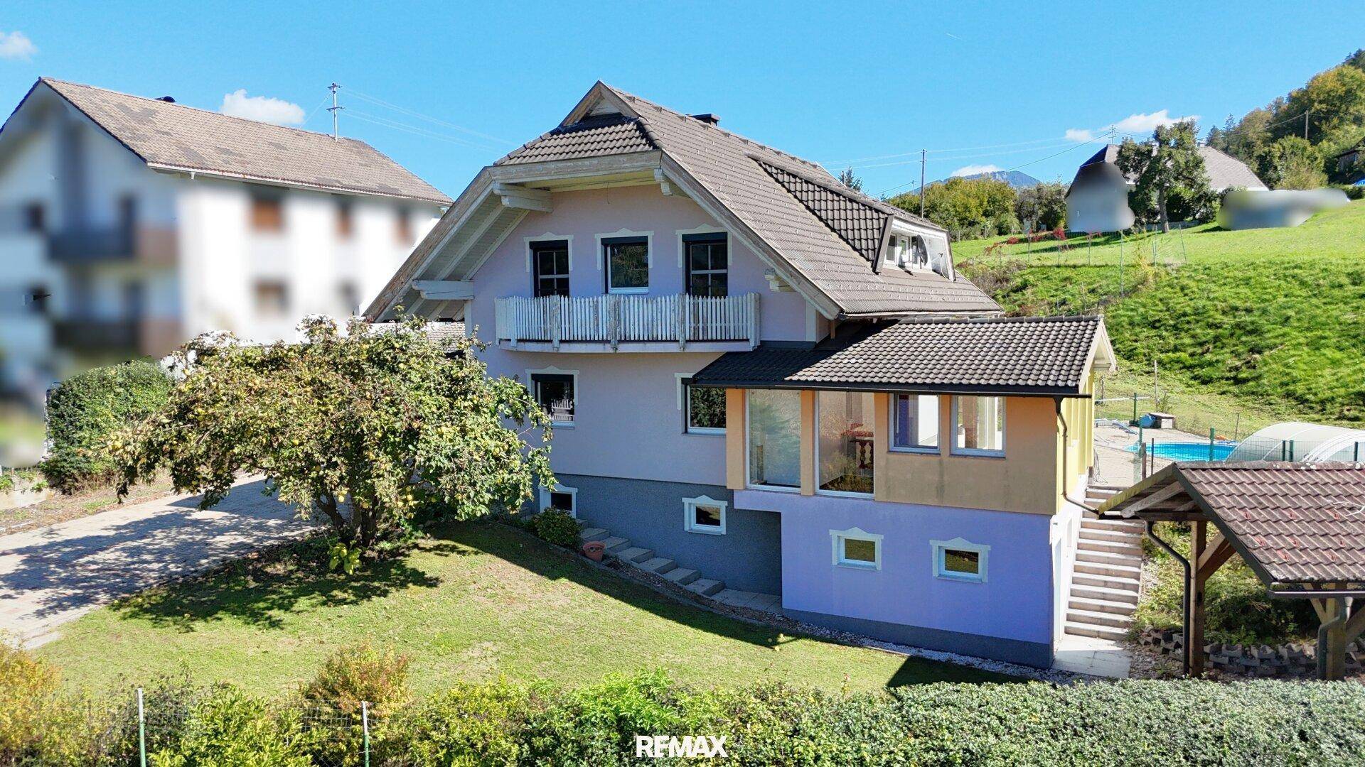 Seitenansicht des Hauses mit Balkon, Garten und Blick auf die grüne Hügellandschaft.