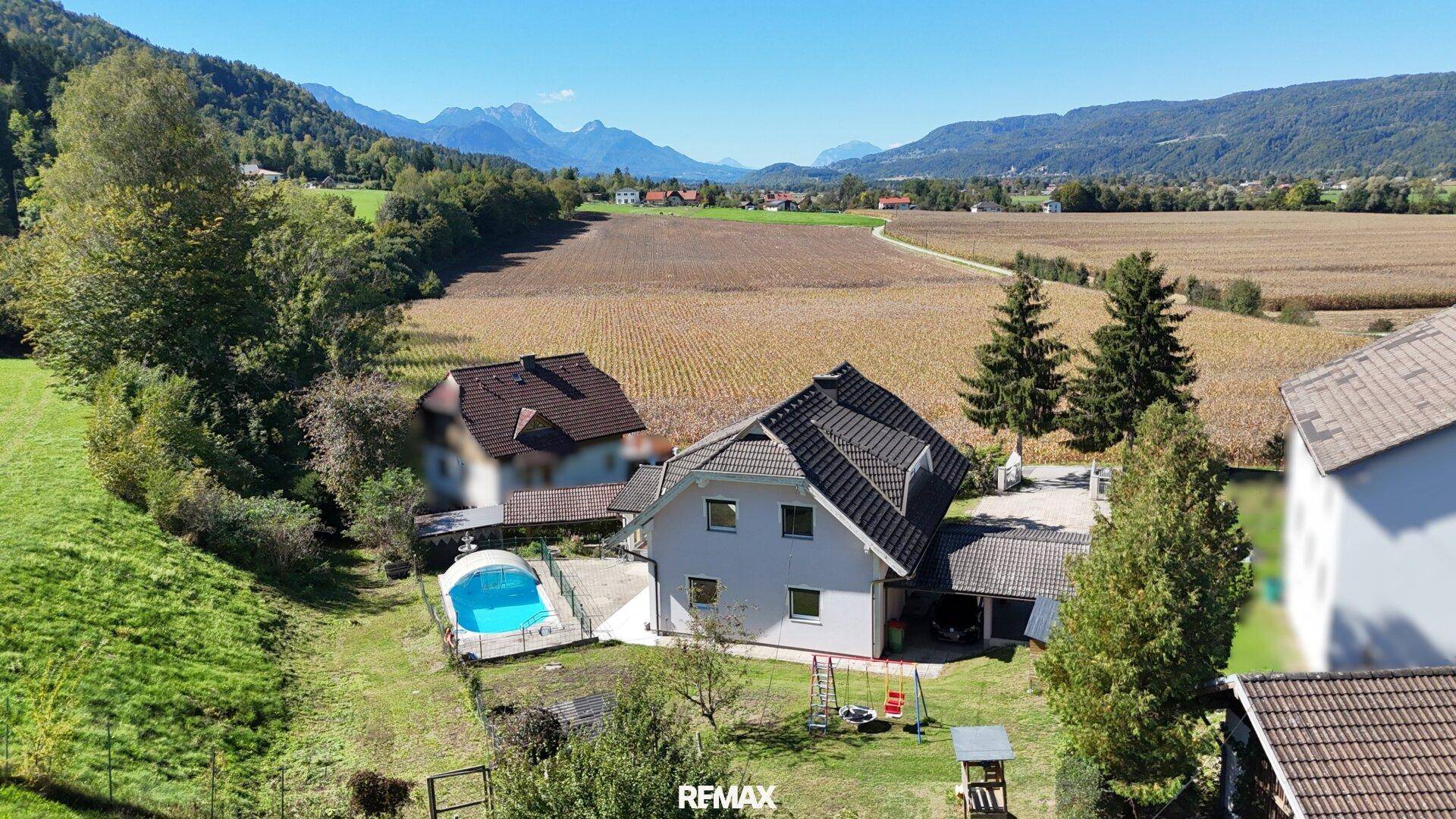 Weitläufige Luftaufnahme des Anwesens mit Pool, Spielplatz und Feldern im Hintergrund.