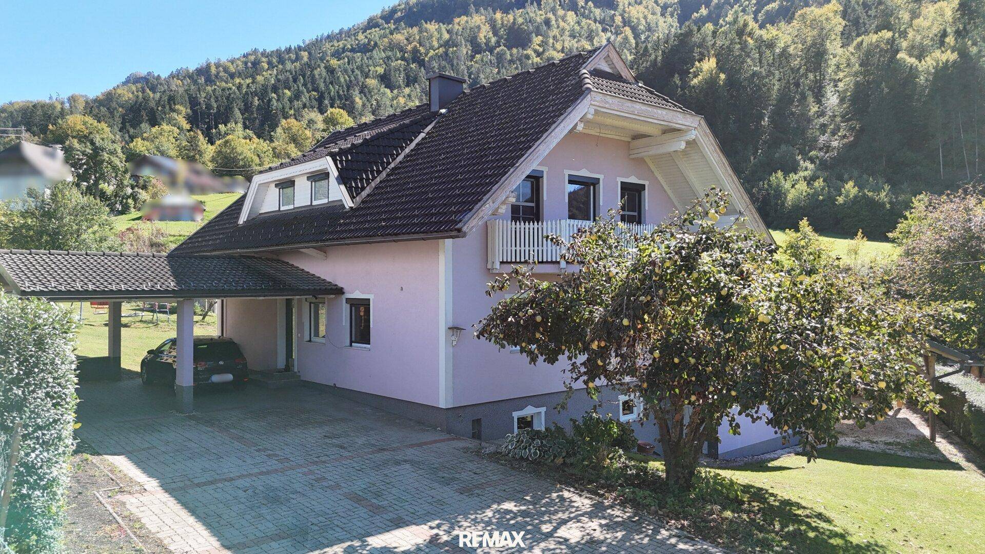 Vorderansicht des Hauses mit Carport, gepflasterter Einfahrt und umgebender Natur.