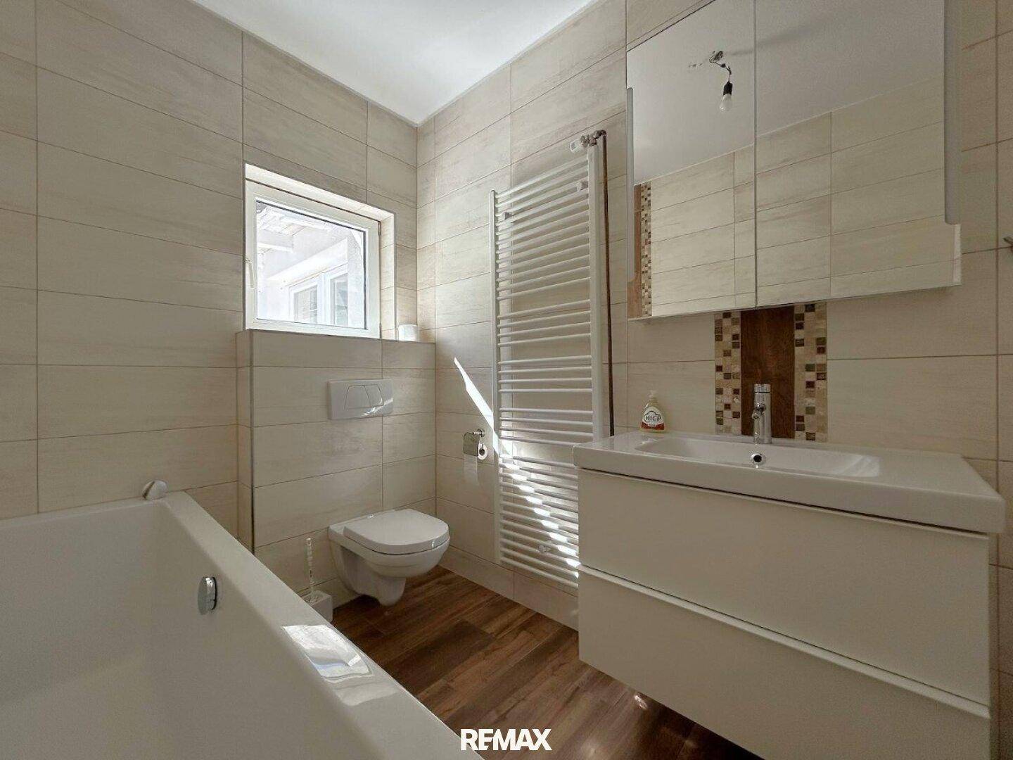 Modernes Badezimmer mit Badewanne, WC, Waschbecken und beheiztem Handtuchhalter.