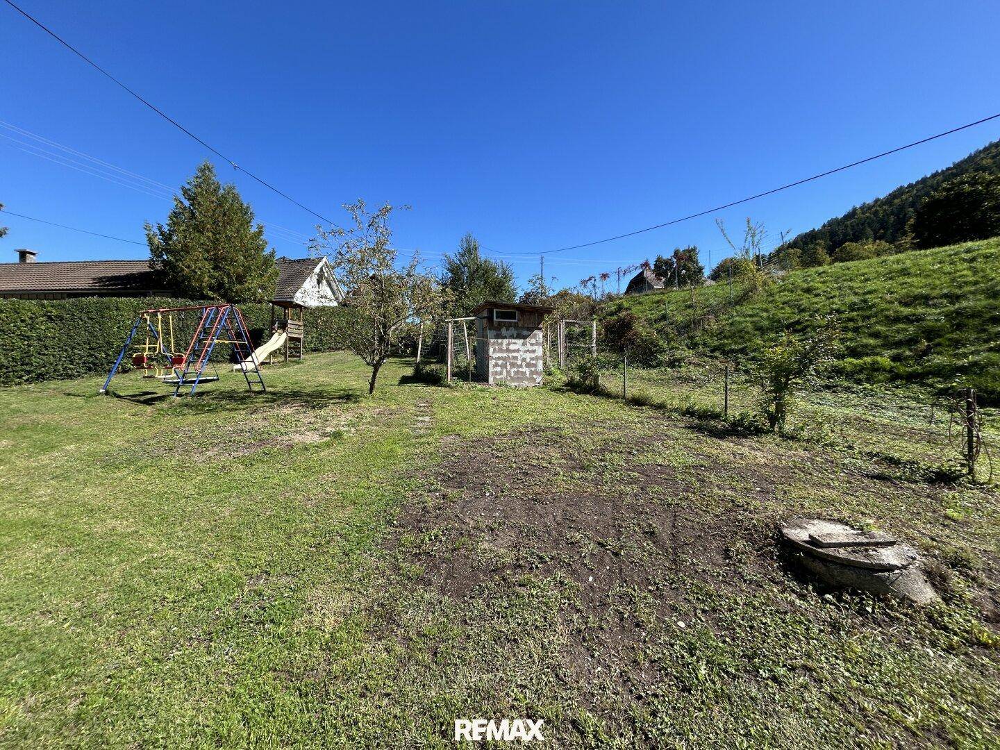 Großer Gartenbereich mit Kinderspielplatz, Gartenhaus und viel Grünfläche am Hang.